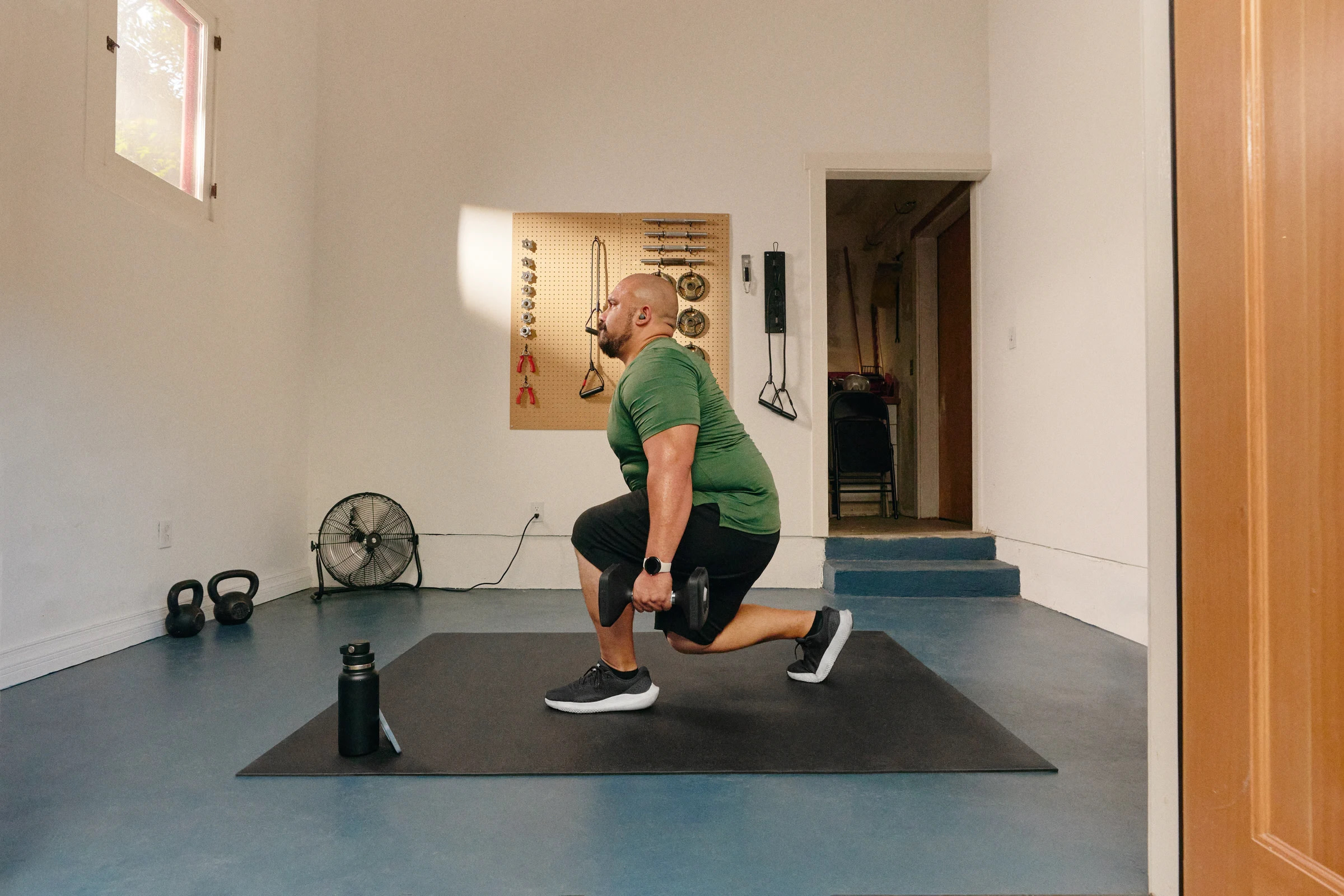 A man does a strength workout in his home gym using the Peloton App.