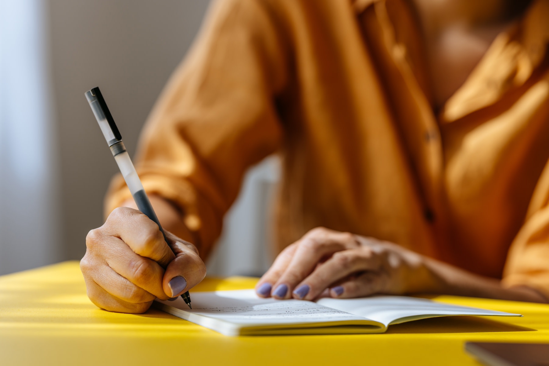 A close-up photo of a woman journaling for mental health with a small notebook and a pen.