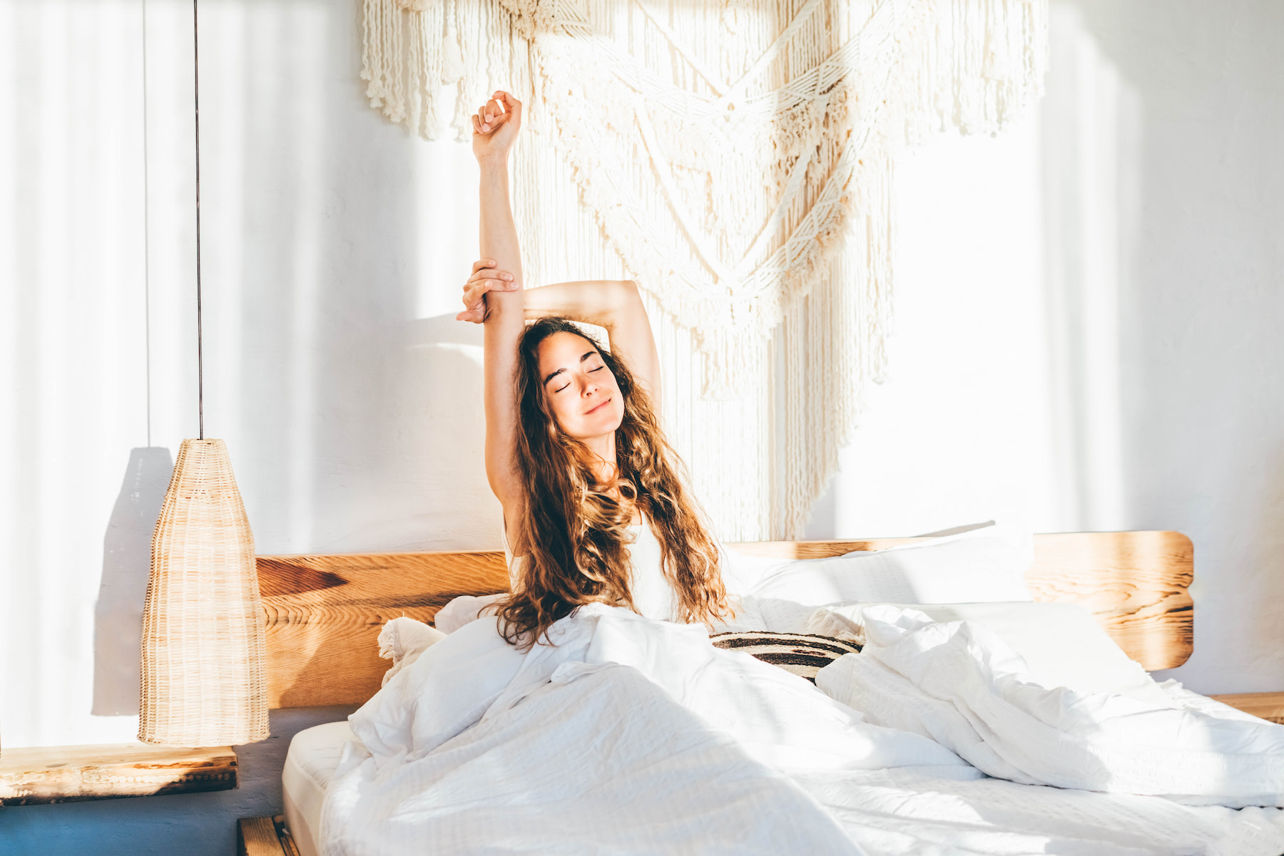 A woman stretching in bed as she wakes up early in the morning.