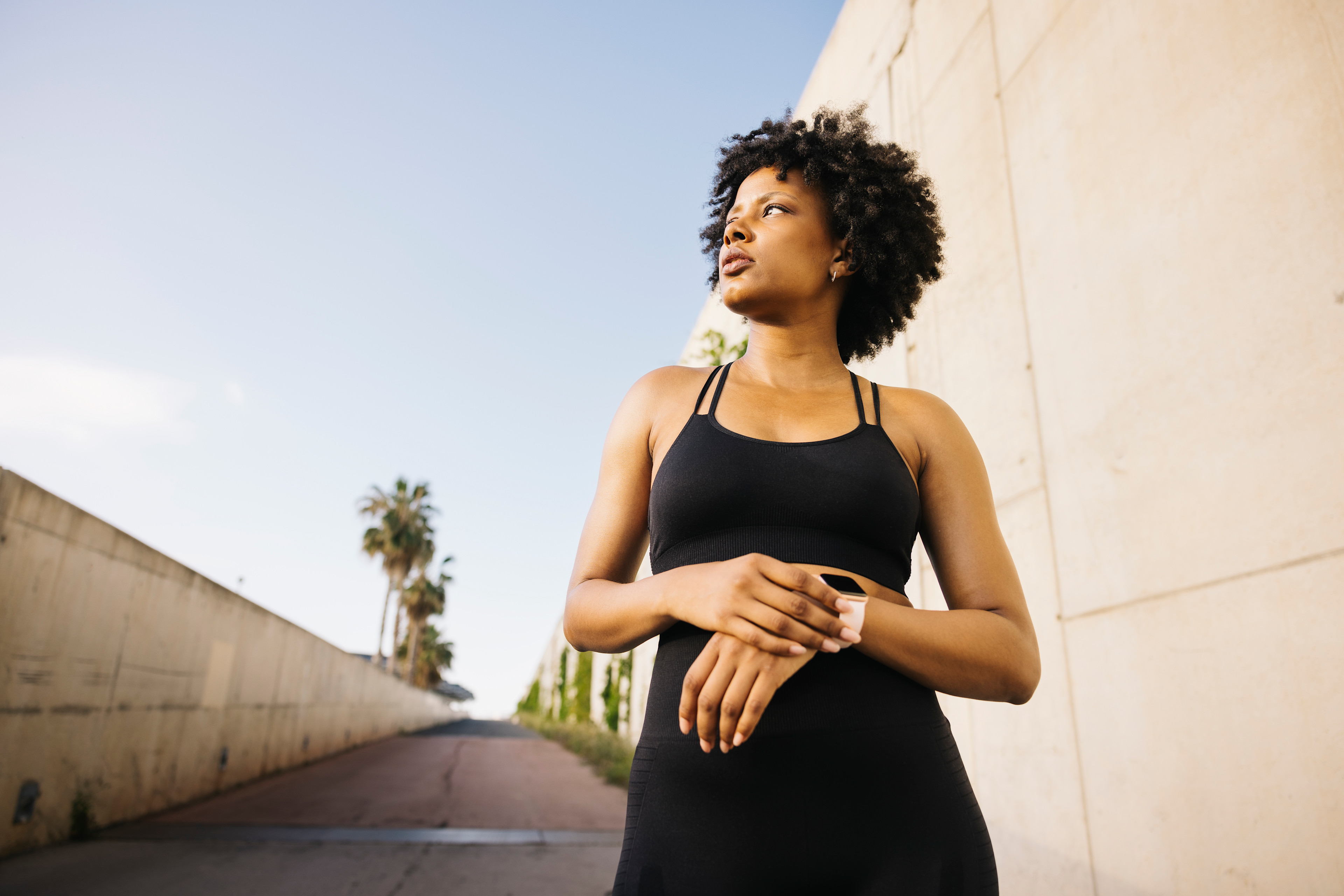 A young woman outside in workout clothes checking her smartwatch deciding whether to run faster or longer