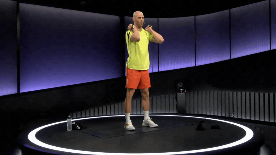 Peloton instructor Marcel Maurer demonstrates a resistance band front squat.