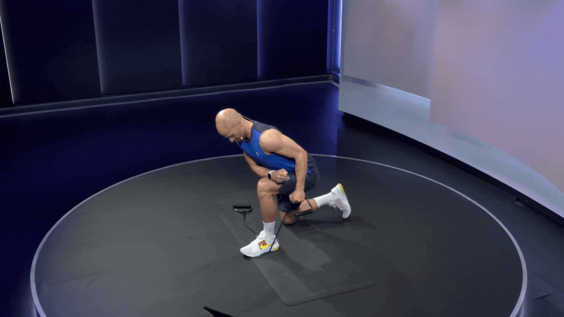 Peloton instructor Marcel Maurer demonstrates a single arm resistance band triceps kickback in a kneeling position
