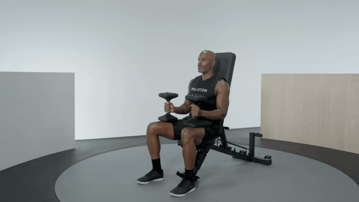 Peloton instructor Adrian Williams demonstrates a seated overhead press with proper form