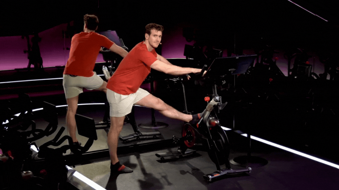 Peloton instructor Bradley Rose demonstrates a standing hamstring stretch on a Peloton Bike
