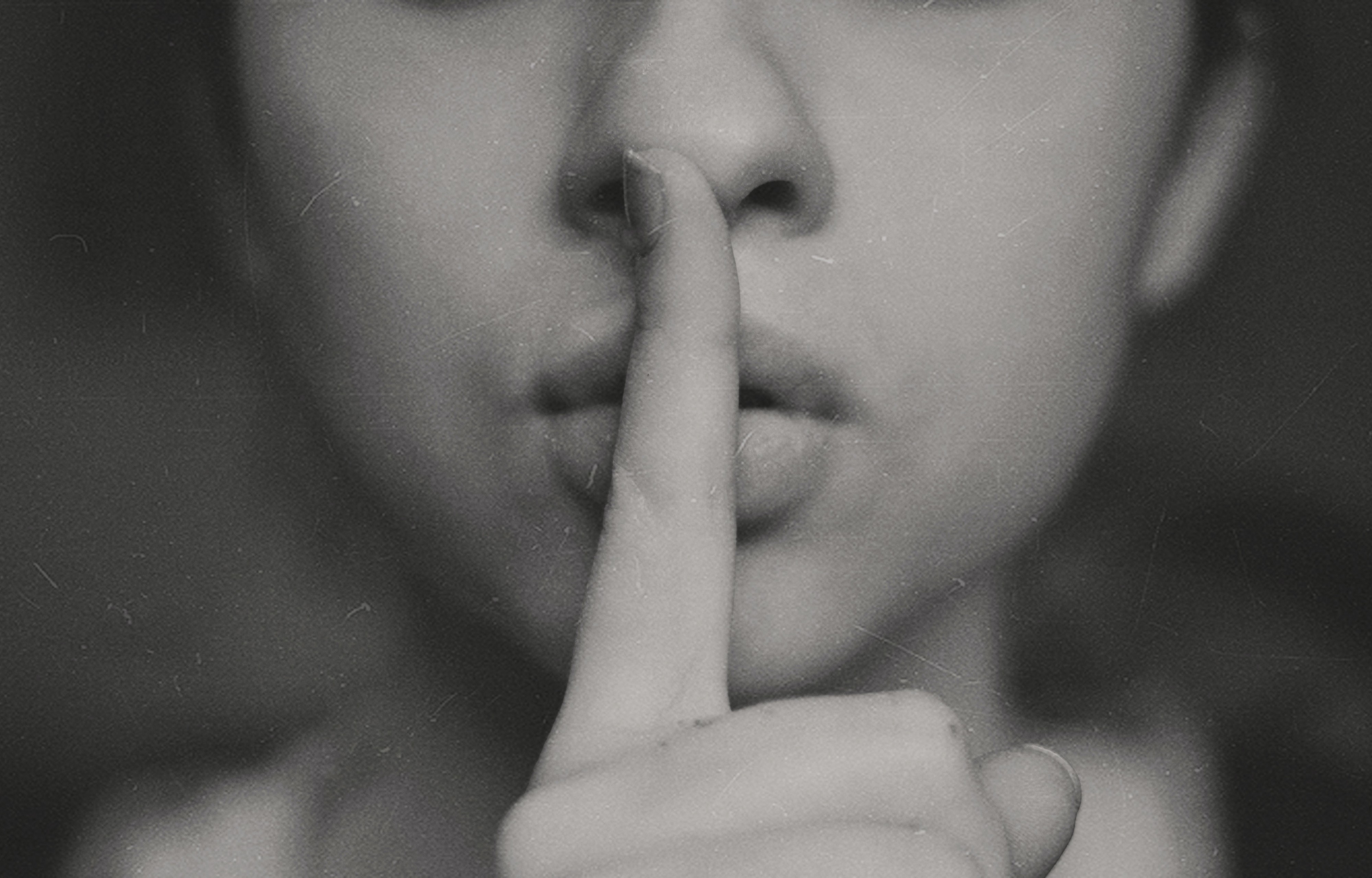 A woman has her finger over her lips in a gesture saying “hush”.