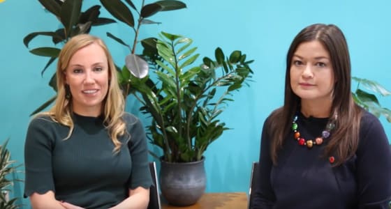 Clare Reilly from PensionBee and Nanvy Kilpatrick from Legal & General sit infront of a turquoise and yellow wall, surrounded by plants.