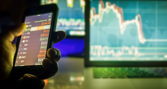 Daytrader in dark using mobile phone and screens with charts