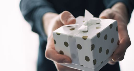 man in blue jumper handing a white present with gold spots to the camera