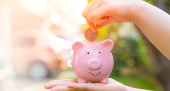 Coin being placed into a pink piggy bank with a bright but blurred background