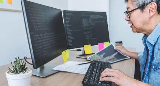 Man sat infront of a computer working and looking at coding