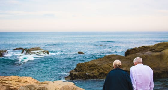 Old couple sitting infront of a cliff edge looking over the sea