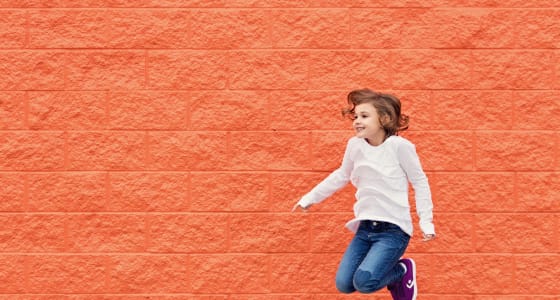 Little girl jumping in front of orange brick wall