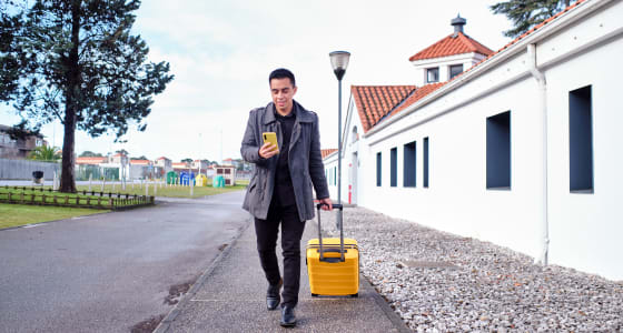 Man on his phone, walking and carrying a suitcase.