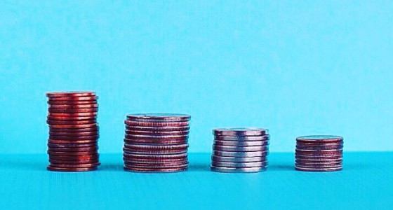 Four small piles of coins stacked against a blue backdrop.