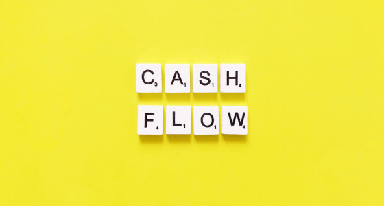 scrabble tiles that spell out cash flow on a yellow background.