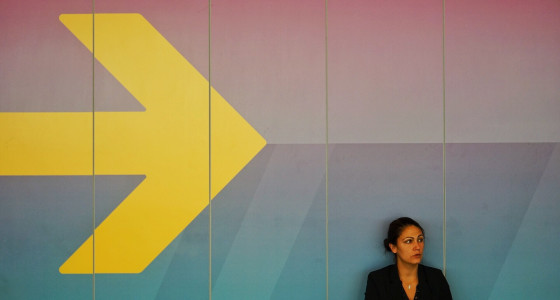 businesswoman sitting against a big yellow arrow in the background.