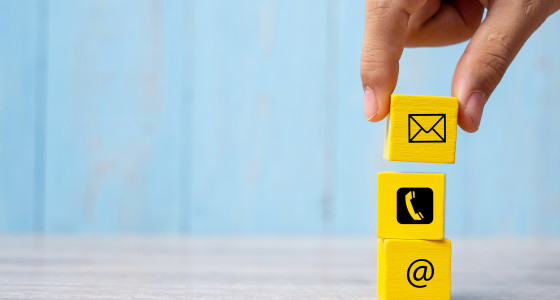 Light blue background with a stack of small yellow blocks with email, phone and @ symbols on