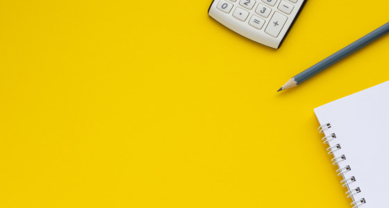 a calculator, pencil and white notepad on a yellow background