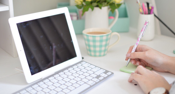 A women writing at a desk with an ipad and keyboard