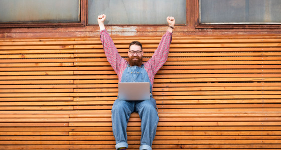 Man raising in his hands in celebration sat over a laptop