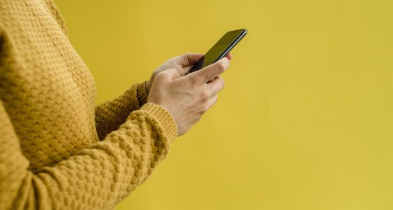 Woman wearing yellow sweater using smartphone.