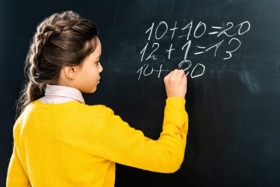 A schoolgirl in yellow jumper writing on a blackboard.