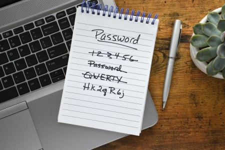 A list of insecure login passwords on a notepad laying on a laptop.