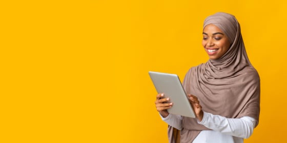 Muslim woman smiles looking at phone against yellow background.