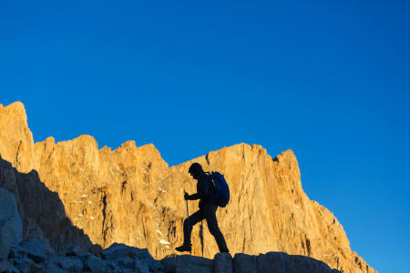 Man climbing a mountain against a blue sky.