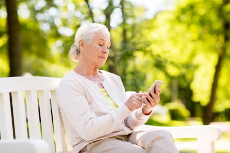 Senior woman sat on park bench looking at phone