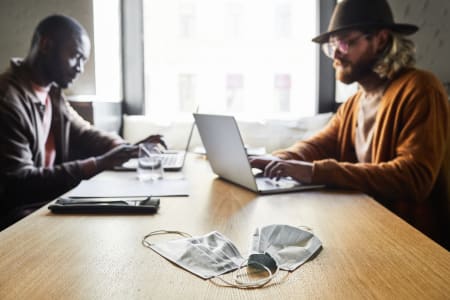 Two men sitting in a cafe on laptops.