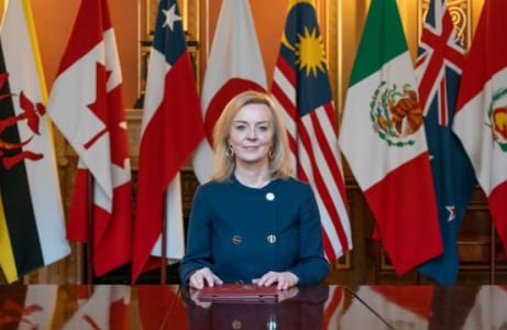 Liz Truss sat at table in front of flags.