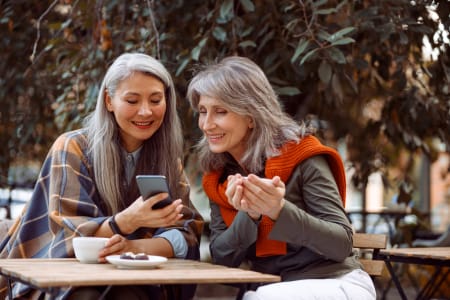 Two older women looking at phone, in outside cafe.