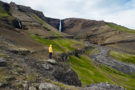 Man standing, wearing yellow jacket, in front of a valley.