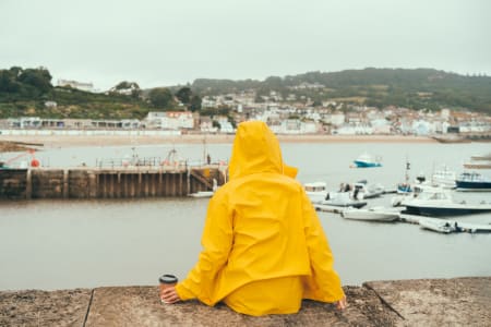 Woman sat, wearing yellow jacket, in front of a sea port.