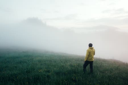 Man standing, wearing yellow jacket, in front of fog across a field.