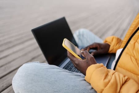 Man working on laptop using yellow cell phone to verify account