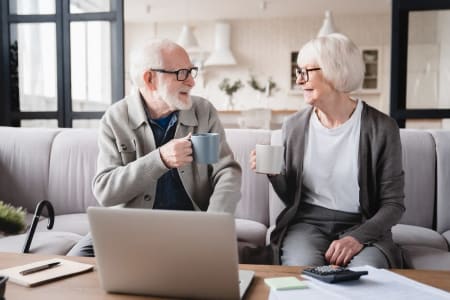 Elderly couple smiling and drinking tea with a laptop in front of them.