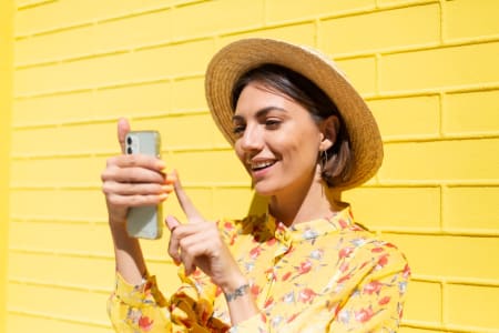 Woman wearing hat looks at phone in the sun