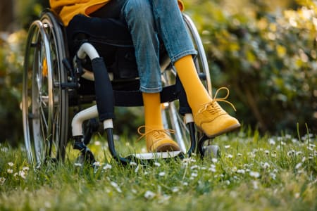 A women in a wheelchair, on grass, wearing mustard shoes and socks.