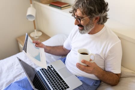 Mature man working with laptop sitting on a bed at home