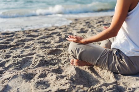 Lady sitting on sandy beach meditating in front of breaking waves