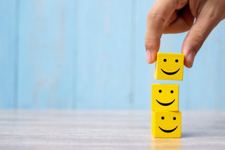 A stack of 3 yellow blocks with a smiley face on infront of a blue background