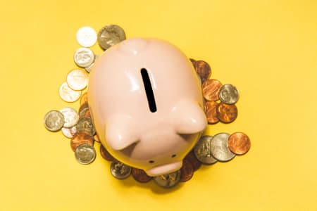 Pink piggy bank sitting on a pile of coins with a yellow background