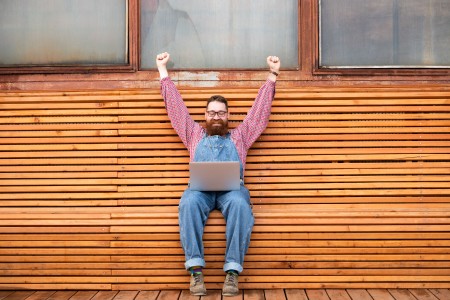 Man raising in his hands in celebration sat over a laptop