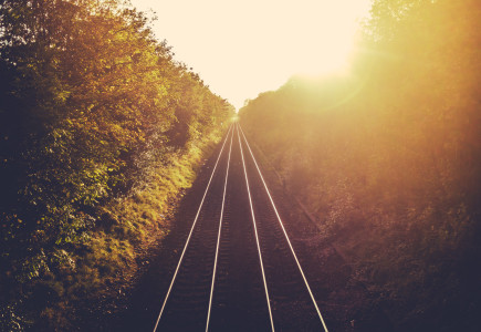 Train tracks at sunset, with trees on each side.