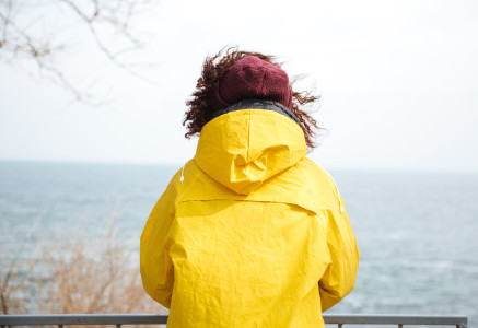 Woman in yellow coat looking out at sea.