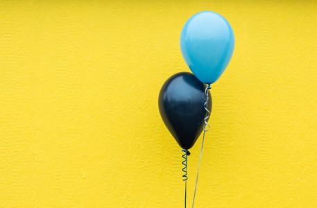 Two balloons floating in front of a yellow wall