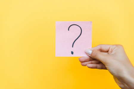 Woman's hand holding pink sticky note with question mark written on it.