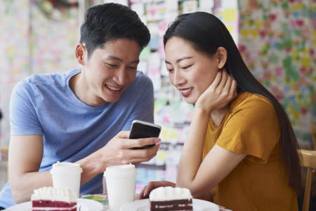 Couple check mobile phone over cake and hot beverages.